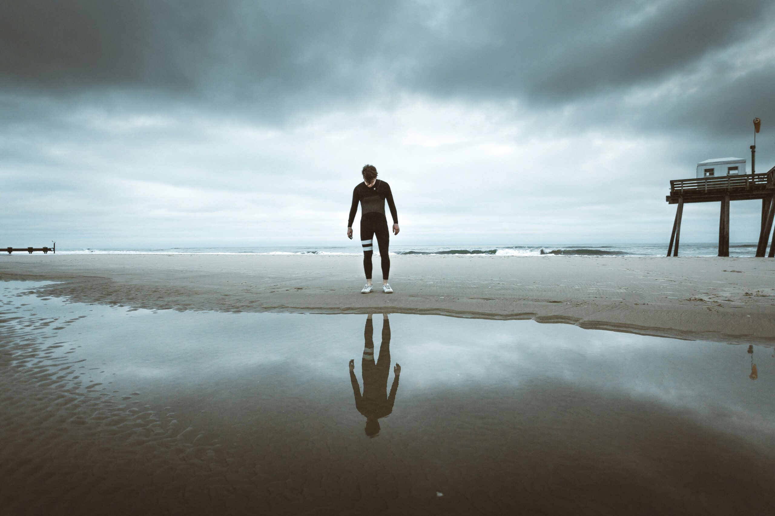 woman in black long sleeve shirt and black pants walking on seashore during daytime